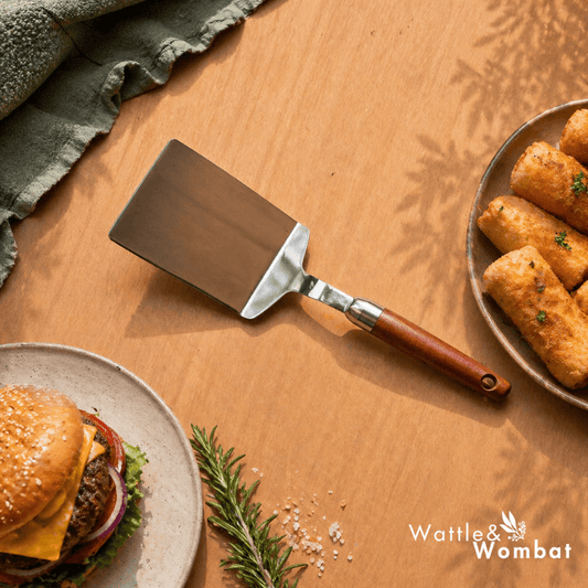 Spatula on a wooden surface with a burger and fries, featuring the Wattle & Wombat logo.